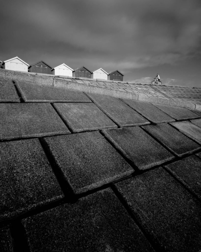 Lucky timing as a cyclists enters the frame. Wide angle photograph of Beach huts in Dawlish Devon