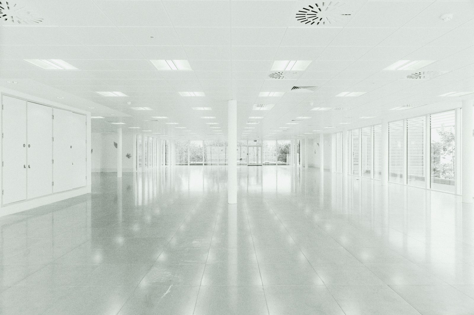 Empty open-plan office after refurbishment, a quiet liminal space with natural light, clean lines and symmetrical architecture.